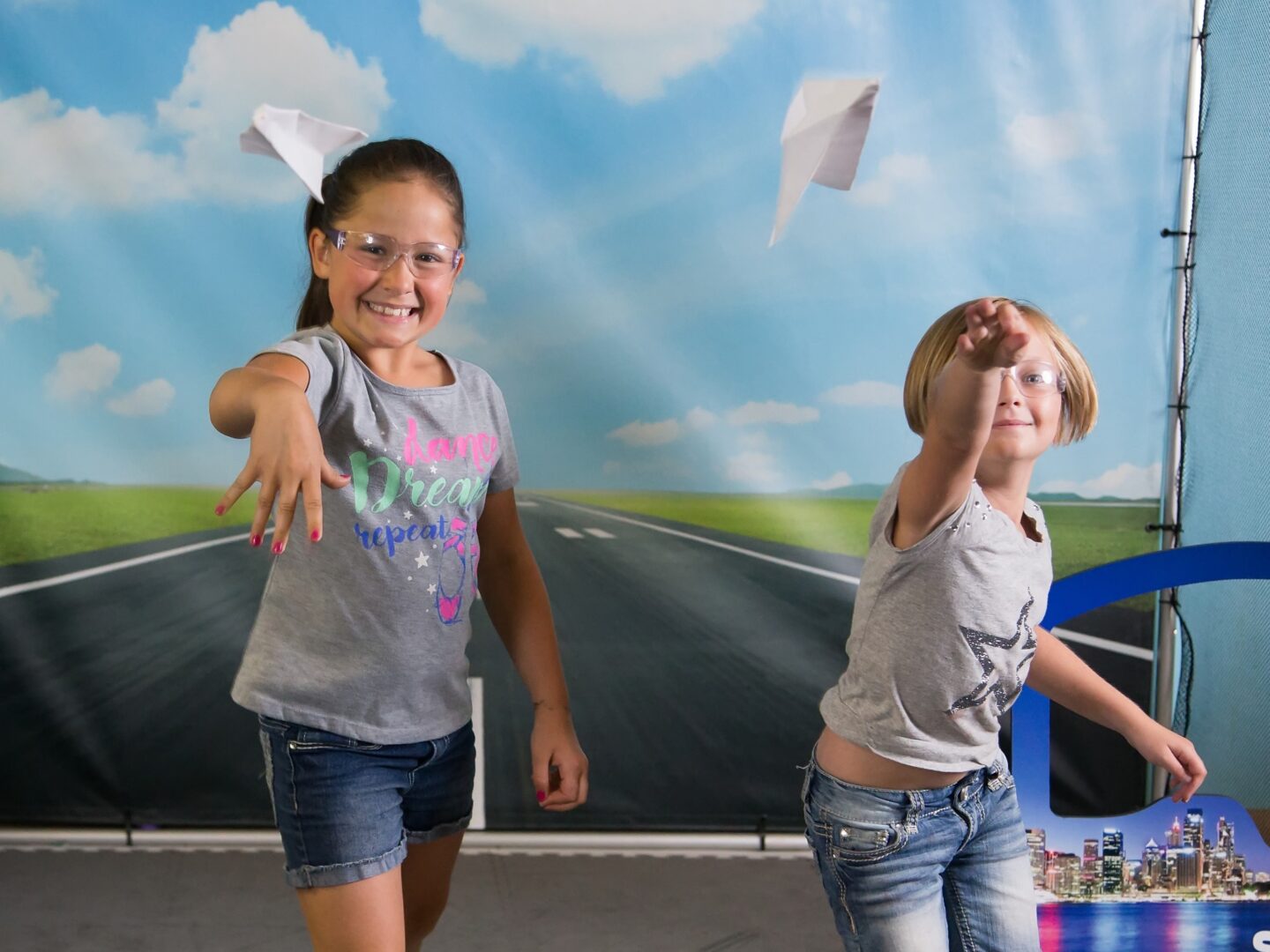 Two girls launch paper airplanes on the runway in Mission Aerospace exhibit