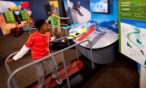 A child is standing on a snowboard simulator in an exhibit.