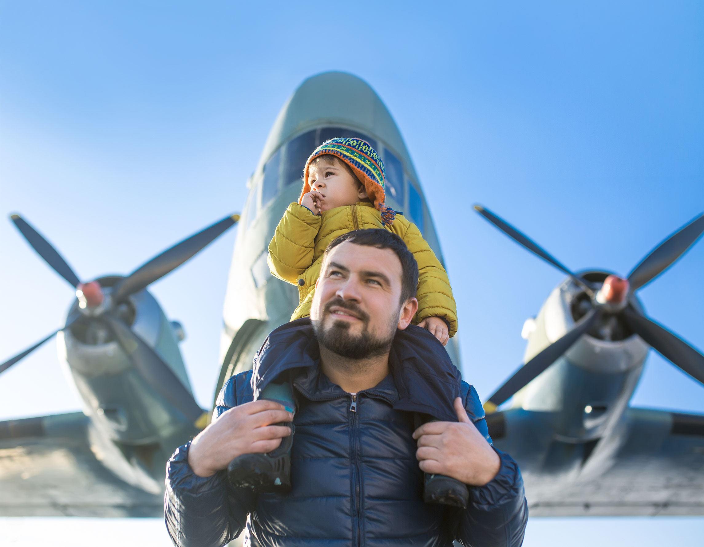 Little boy on dad's shoulders in front of airplane