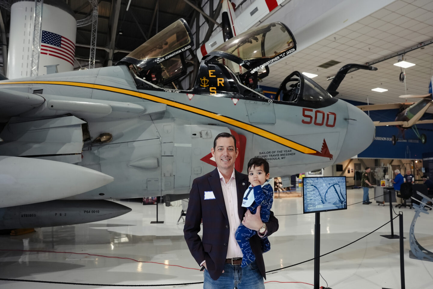 A man is holding his baby in front of the EA-6B Prowler at the Air & Space Museum