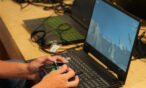 Hands holding a remote controller in front of a laptop. The laptop has a simulation on it.