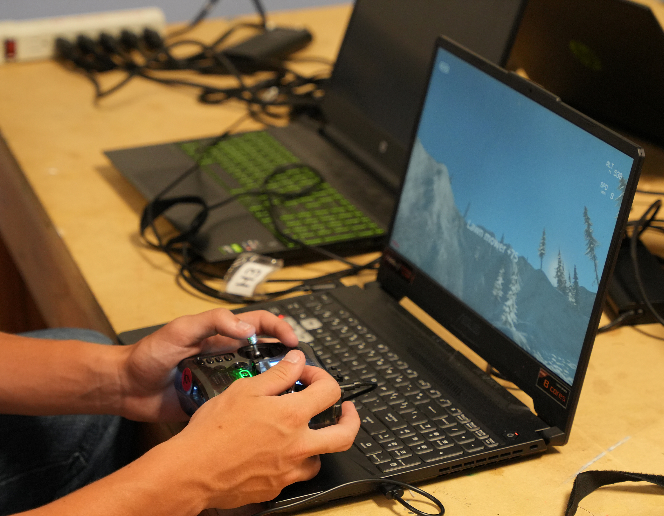 Hands holding a remote controller in front of a laptop. The laptop has a simulation on it.